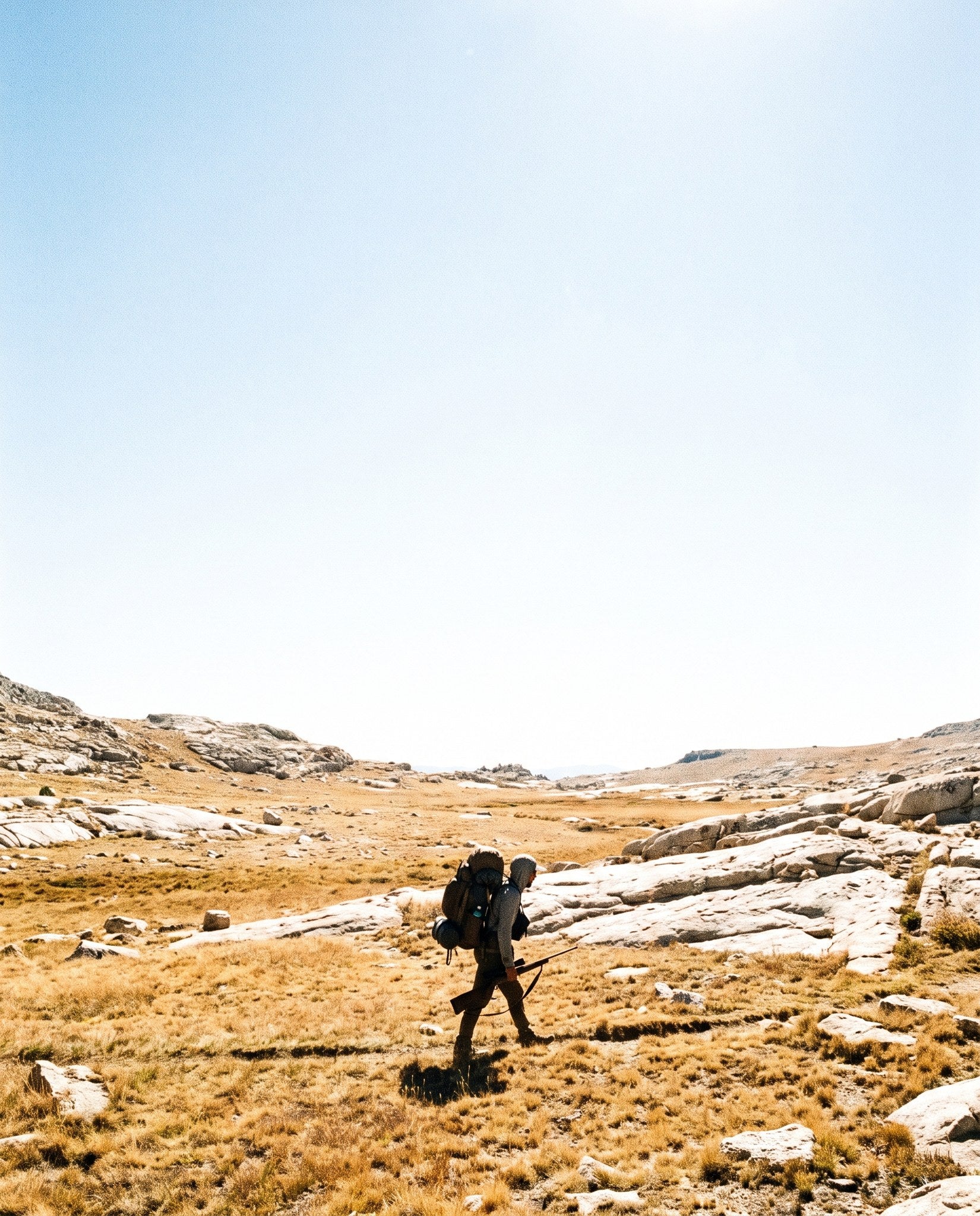 Backcountry hunter crossing an open alpine basin in late season
